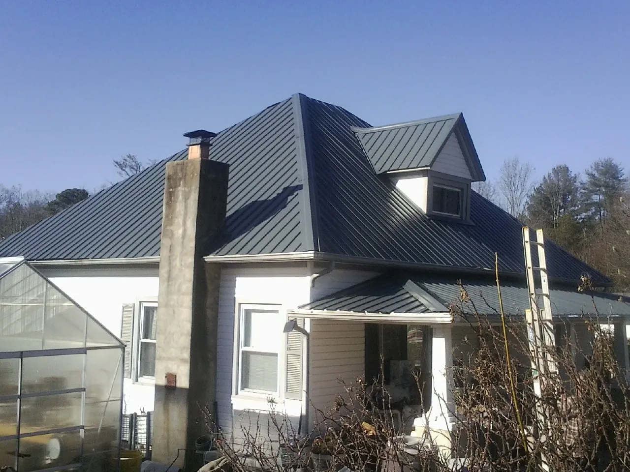Dark blue standing seam metal roof on a white farmhouse with dormer — Slate & Tile Roof Repair by Roofing Brothers in Austinville