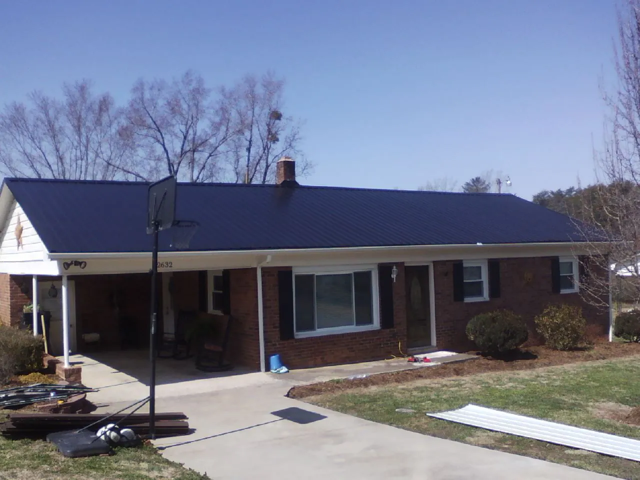 Finished dark blue metal roof on a brick ranch with a carport in Austinville
