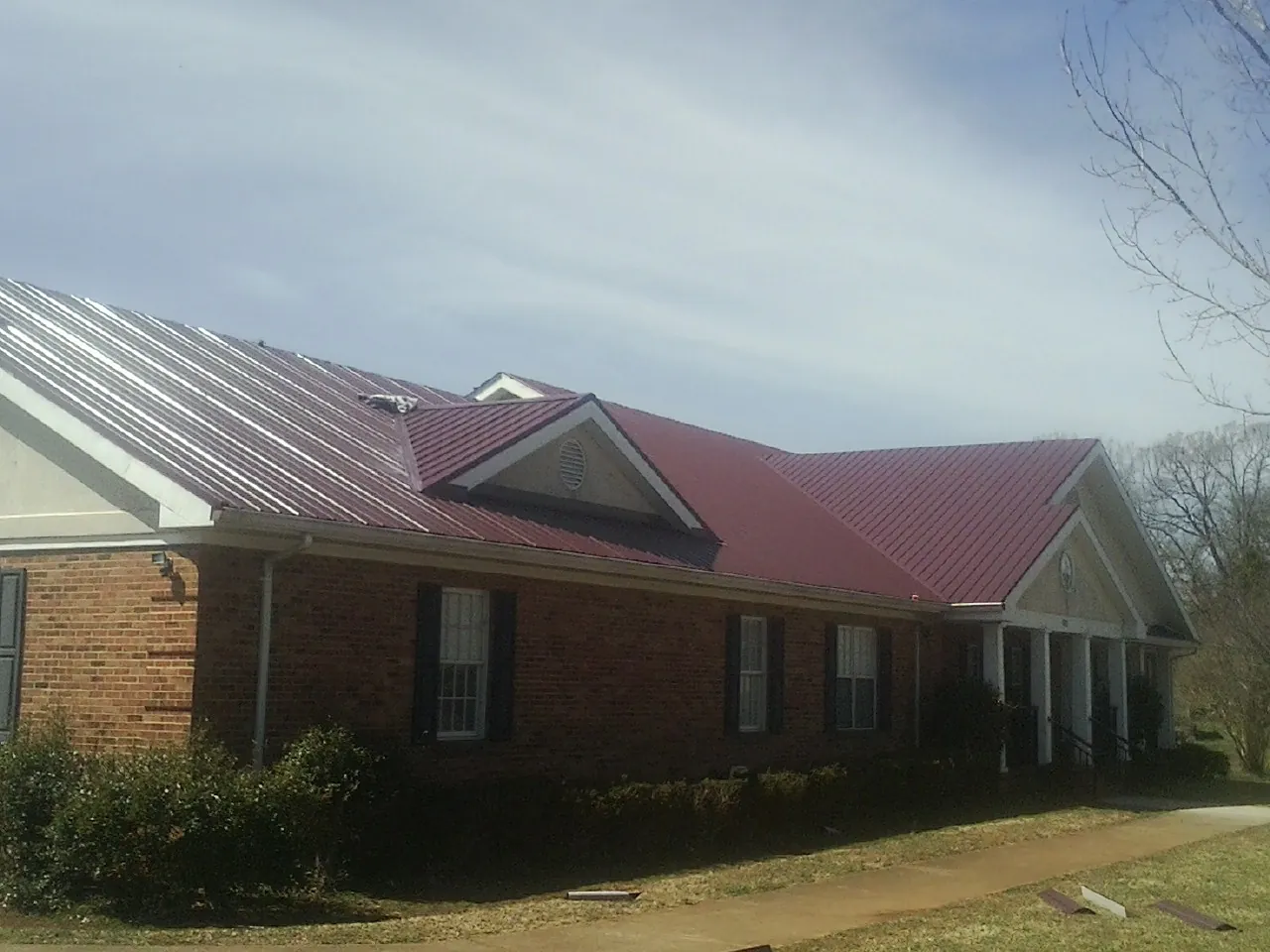 Red metal roof with gabled entries on a long brick building, from a Hail Damage Roof Repair job in Austinville