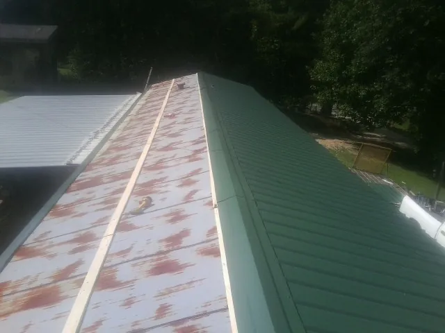 Old rusted panels beside newly installed green metal roofing — Wind Damage Roof Repair by Roofing Brothers in Austinville