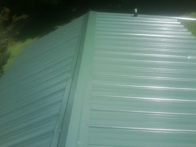 New green metal panels meeting at the ridge of a roof — Flat Roof Repair work by our crew in Austinville