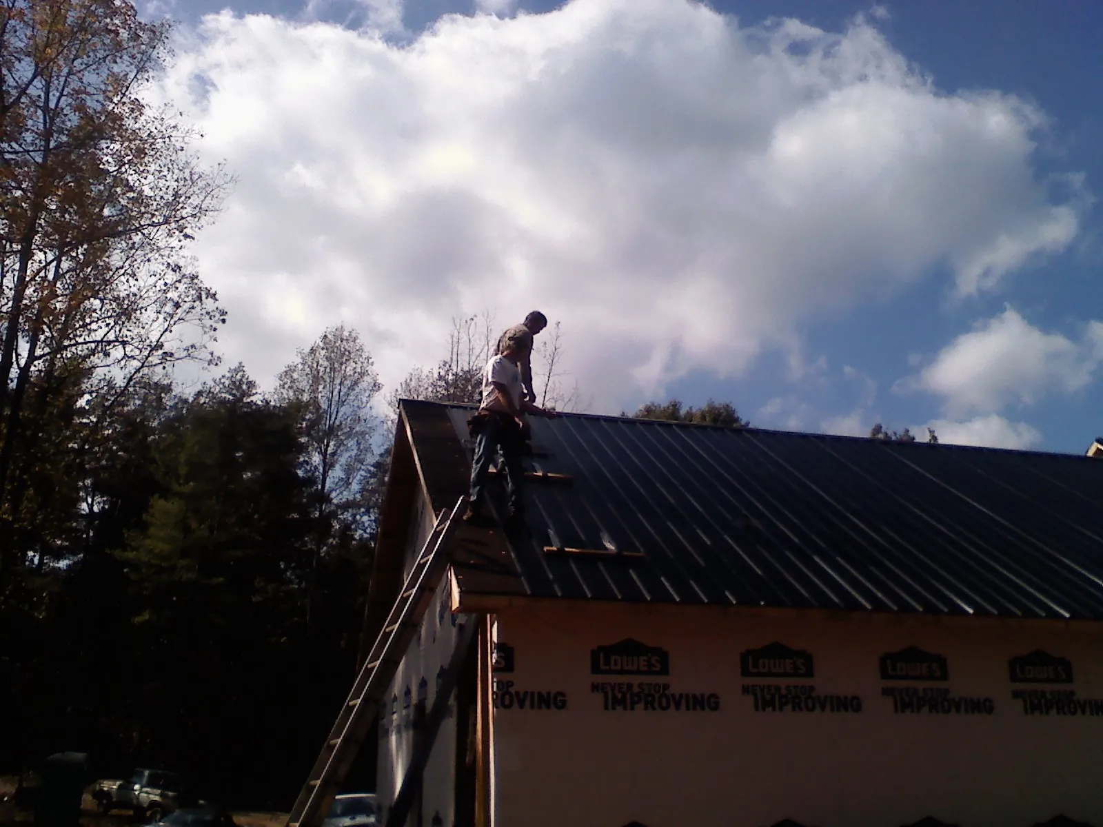 Roofer fastening dark metal panels high against a cloudy sky, from a Roof Inspection job in Austinville