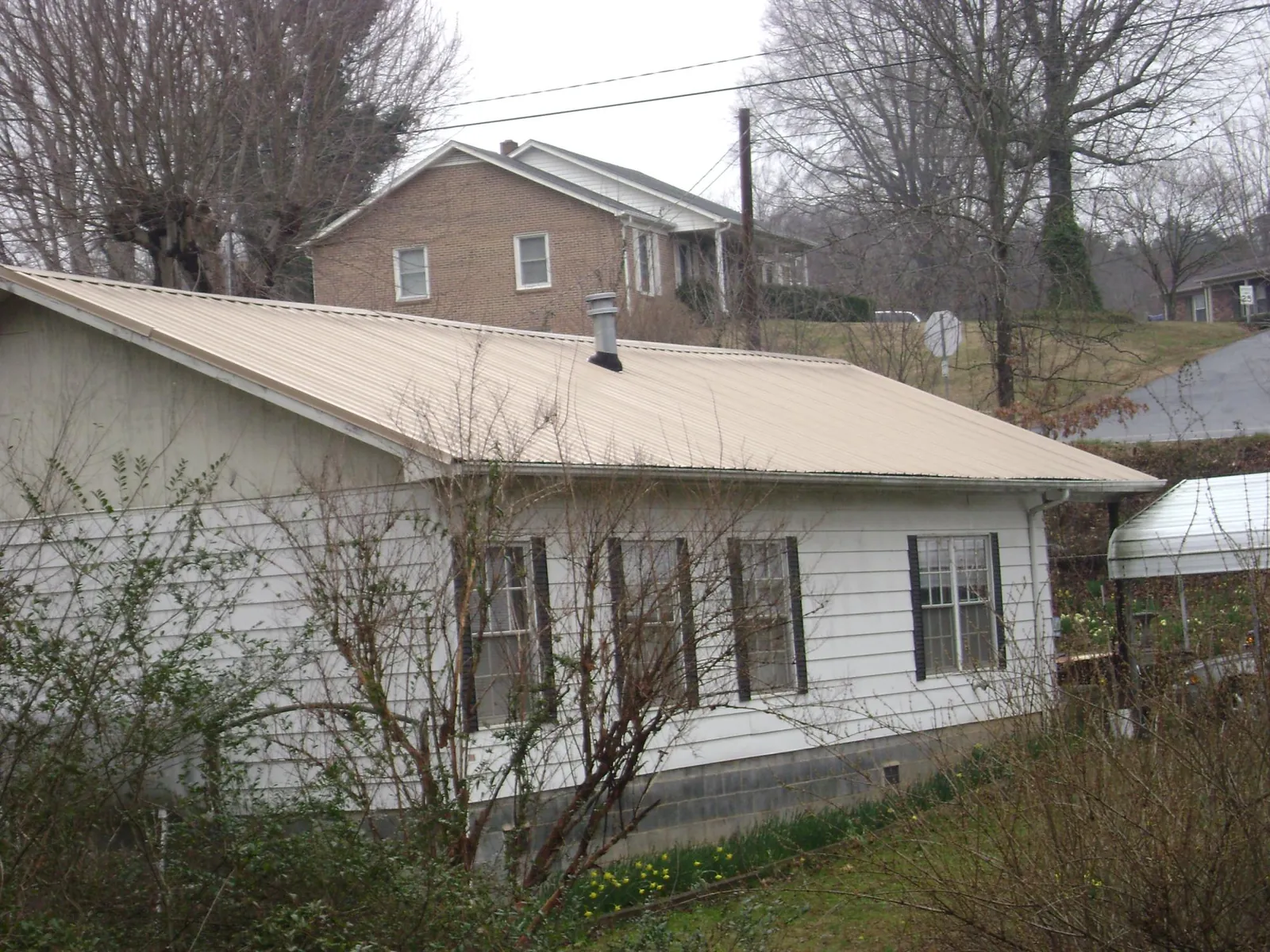 Tan metal roof on a white sided house set into a hillside — Commercial Roofing by Roofing Brothers in Austinville