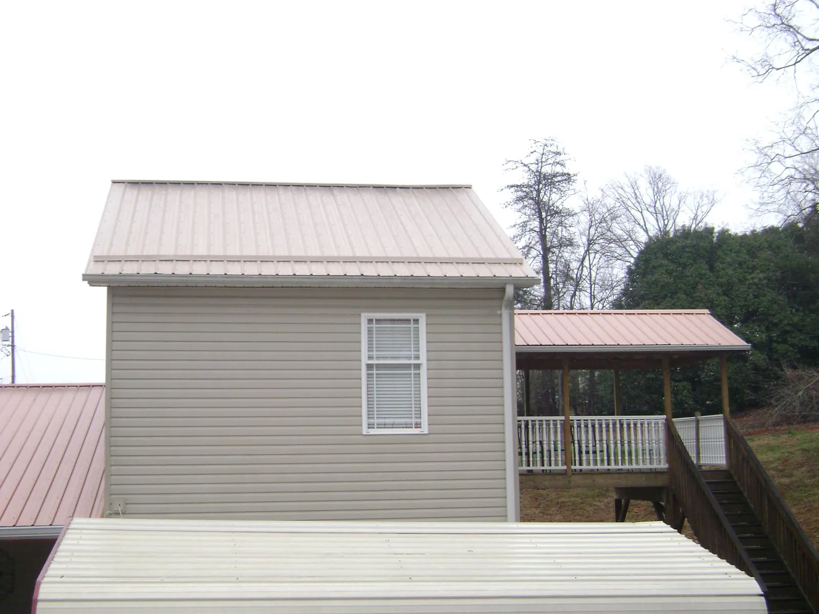 Tan metal roofs on a two story addition and attached porch, from a Roof Replacement job in Austinville